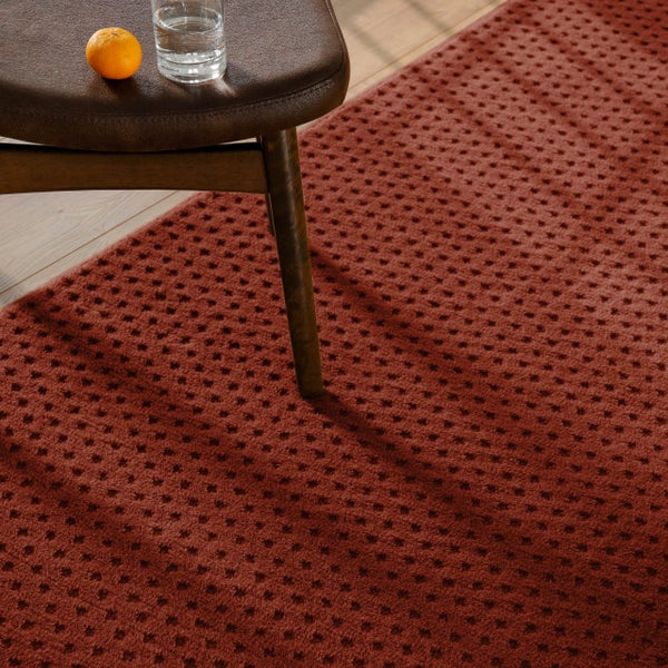 Strukturierter rotbrauner Teppich mit Punktmuster unter einem Hocker auf Holzfußboden.