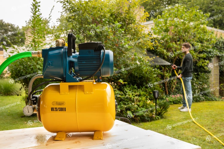 Hauswasserwerk mit gelbem Tank im Garten, ein Mann bewässert Pflanzen