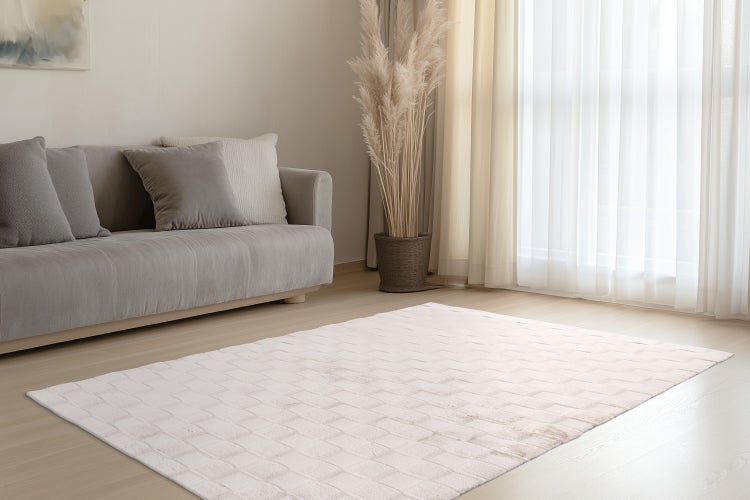 Helles Wohnzimmer mit rechteckigem Teppich in strukturierter Optik, Sofa mit Kissen, Zimmerpflanze und Vorhängen vor einem Fenster.