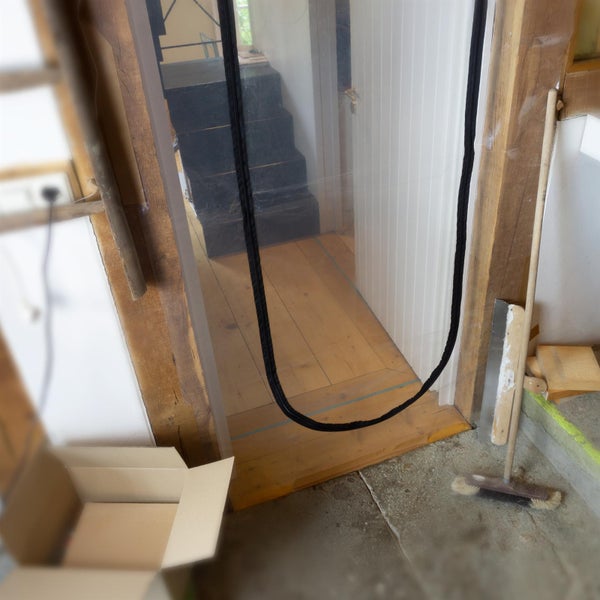 Transparente Staubschutztür mit schwarzem U-Reißverschluss in einem Türrahmen aus Holz bei Renovierungsarbeiten.