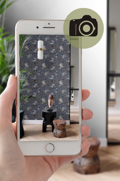 Smartphone zeigt ein Zimmer mit blumiger Tapete, Stehlampe und Dekoration