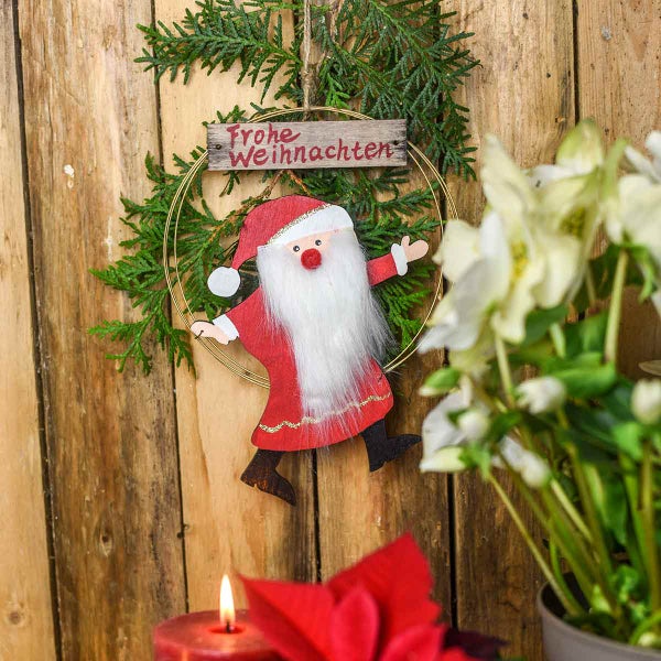 Weihnachtsdekoration mit Tannengrün, Holzschild mit der Aufschrift Frohe Weihnachten und Weihnachtsmannfigur