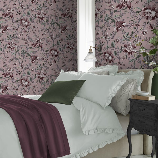 Schlafzimmer mit blumiger Mustertapete und einem Bett mit Kissen sowie einer Decke in einem eleganten und wohnlichen Ambiente.