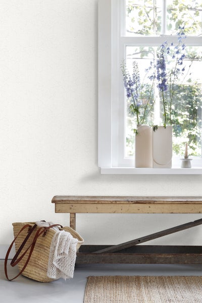 Heller Raum mit gemusterter Tapete, Fenster mit Dekoration, Holzbank und geflochtener Tasche.