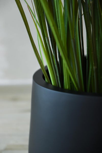 Künstliches Gras in einem mattschwarzen Blumentopf, Detailaufnahme.