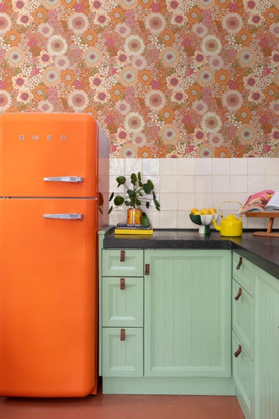 Küche im Retro-Stil mit einer gemusterten Blumentapete, hellgrünen Küchenschränken mit Ledergriffen und einem auffälligen Kühlschrank von Smeg.