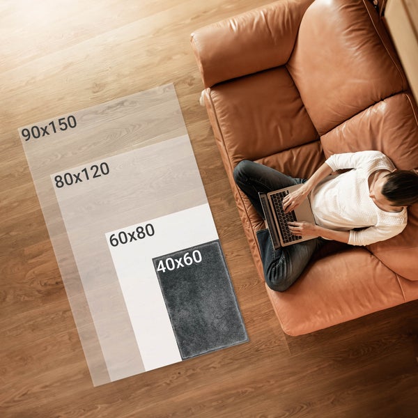 Verschiedene Teppichgrößen von 40x60 bis 90x150 neben einem Mann mit Laptop auf einem Sofa.