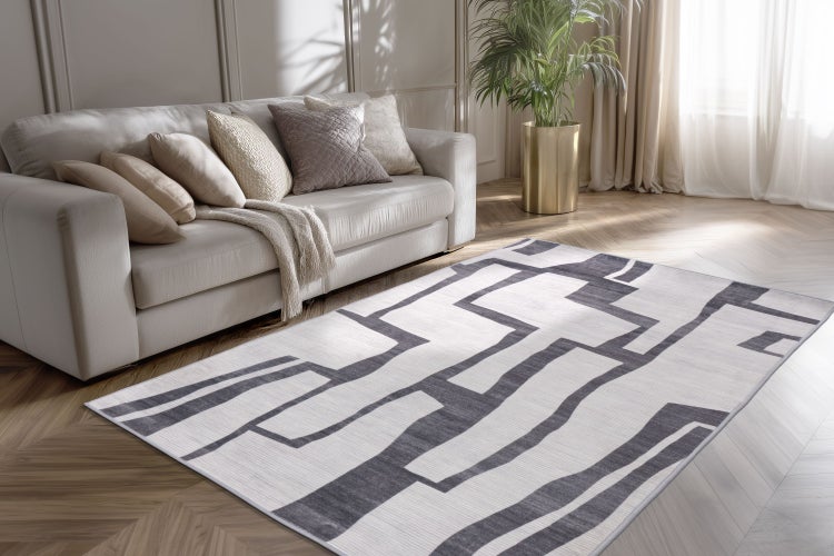 Moderner Wohnzimmerteppich mit geometrischem Linienmuster vor einem hellen Sofa in einem hellen Wohnraum mit Parkettboden.