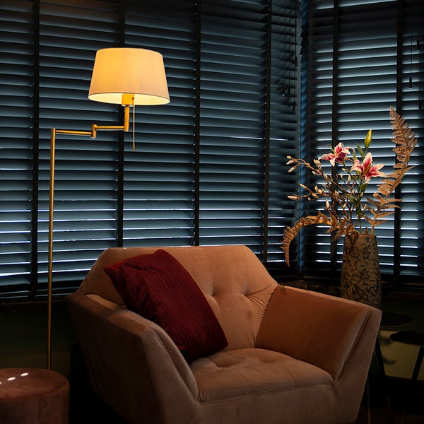 Szene mit Sessel, Stehlampe und Dekoration vor einem Fenster mit Jalousien