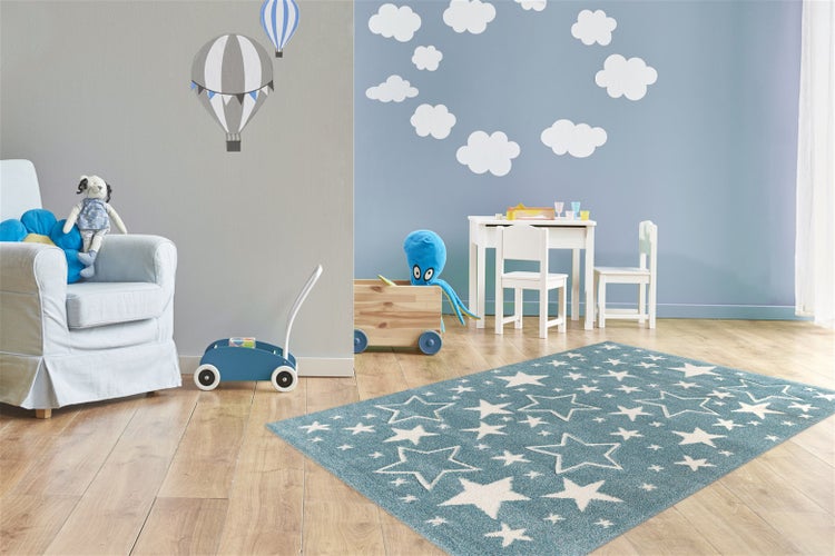 Ein Kinderzimmer mit einem Teppich mit Sternenmuster, einem Kindertisch und Stühlen, einem Spielzeugwagen und einem Sessel.
