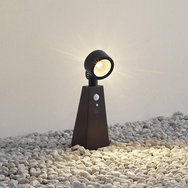 Außenstrahler mit Bewegungsmelder und verstellbarem Lichtkopf, batteriebetrieben, stehend auf Kieselsteinen.