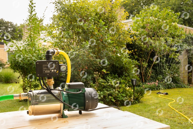 Hauswasserwerk im Garten mit Pumpe, Druckschalter und Schläuchen auf einem Holztisch.