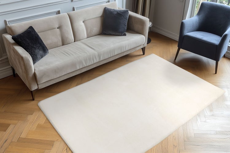 Wohnzimmer mit Sofa, Sessel und modernem Teppich auf einem Fischgrätparkettboden in einem hellen und stilvoll eingerichteten Innenbereich.