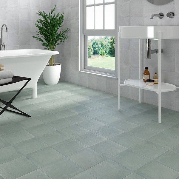 Modernes Badezimmer mit quadratischen Bodenfliesen in Zementoptik, freistehender Badewanne, Waschbecken und Pflanzen in einem hellen Raum.
