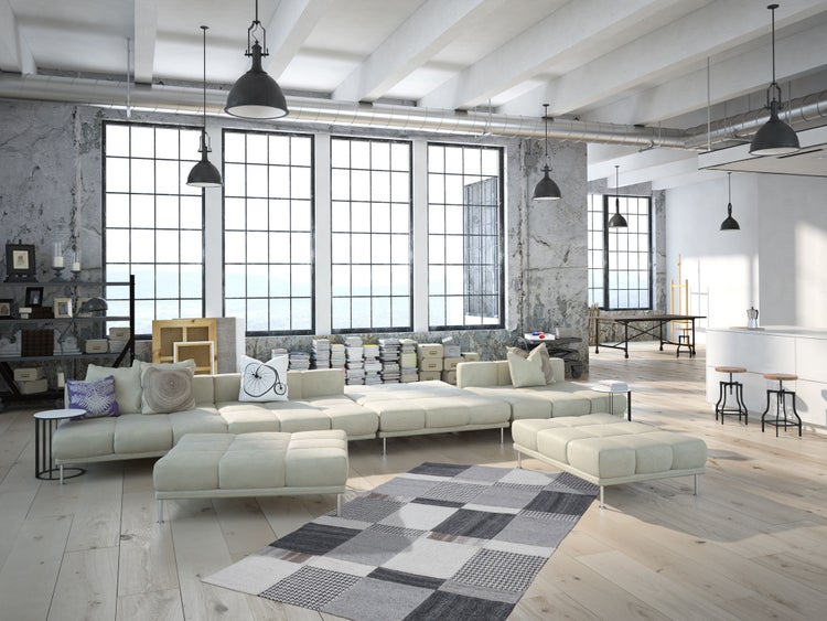 Geräumiges Loft im Industriestil mit offener Wohnküche, großem Sofa, hohen Fenstern, Betonwänden und Holzboden.