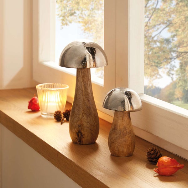 Dekorative Pilzfiguren aus Holz und Metall auf einer Fensterbank mit Kerze und Herbstdekoration