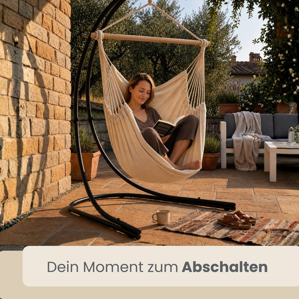 Frau liest ein Buch in einem Hängesessel mit Metallgestell auf einer Terrasse im Freien.
