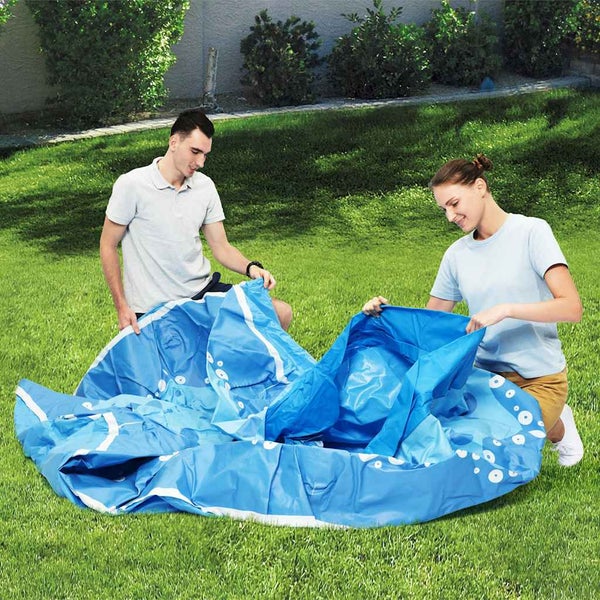 Zwei Personen breiten einen blau gemusterten aufblasbaren Pool auf einer grünen Rasenfläche im Garten aus.