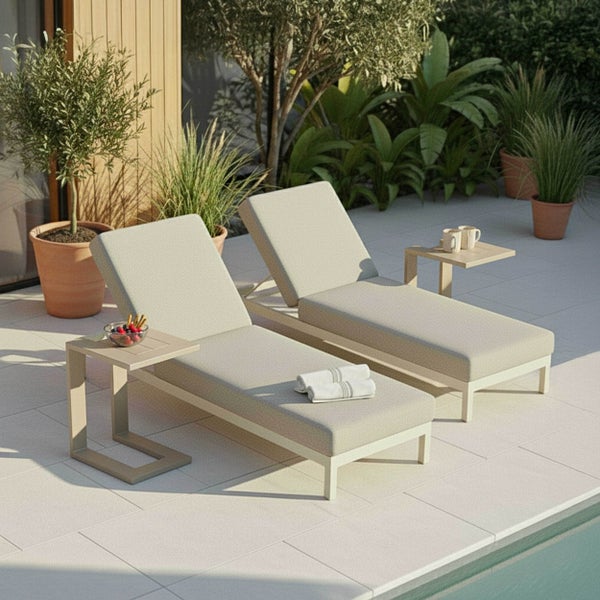 Zwei moderne Sonnenliegen mit hellen Auflagen und Beistelltischen auf einer Terrasse am Pool, umgeben von Grünpflanzen.