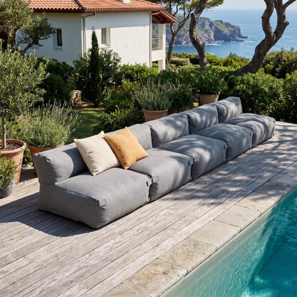 Modulares Outdoor-Sofa auf einer Holzterrasse neben einem Pool in einem hellen Garten mit Meerblick.