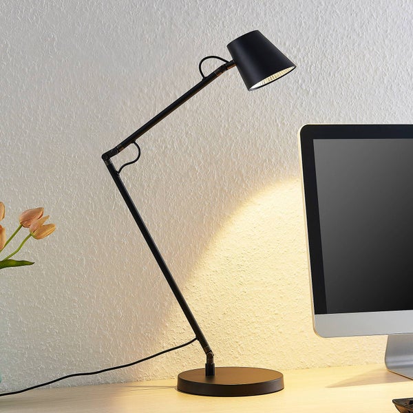 Schwarze verstellbare Schreibtischlampe mit konischem Schirm auf einem Holzschreibtisch neben einem Monitor.