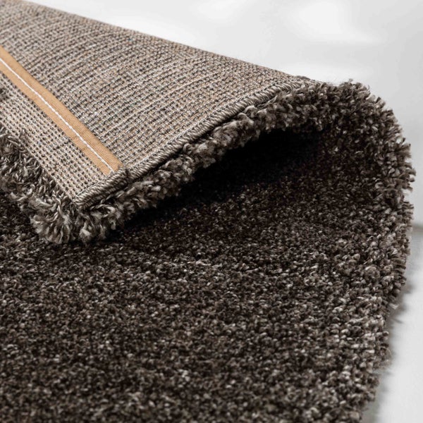 Detailansicht eines braunen Hochflor-Teppichs mit sichtbarem Textilrücken und dichter Florstruktur.