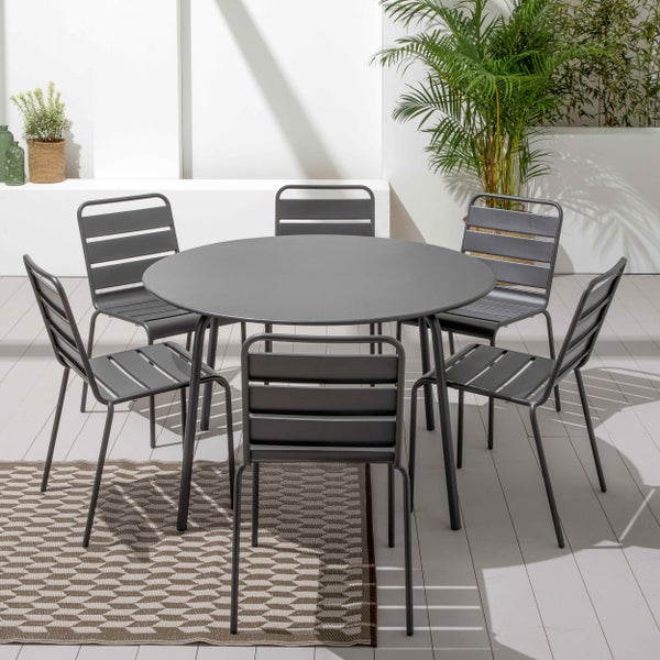 Modernes Gartenmöbel-Set mit rundem Metalltisch und sechs passenden Stühlen auf einer hellen Terrasse mit Pflanzen und einem Musterteppich.