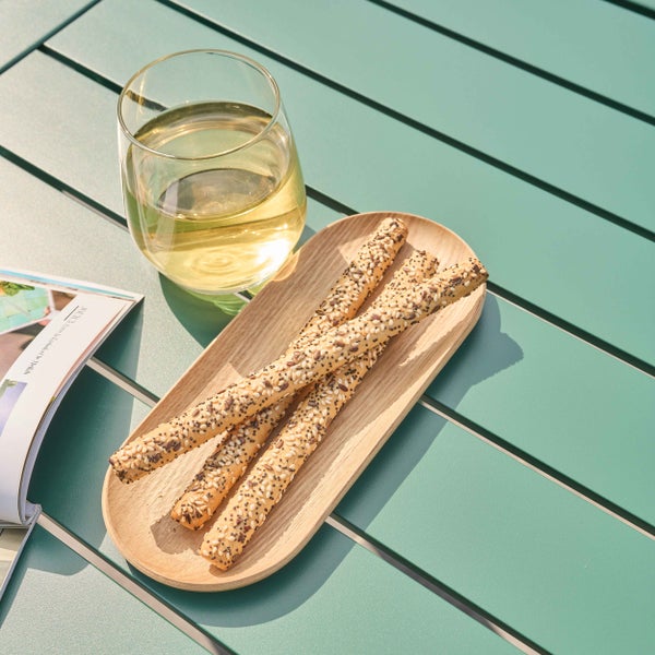 Grüner Gartentisch in Lattenoptik mit einem Glas Wein und einer Holzschale mit Knabbergebäck.