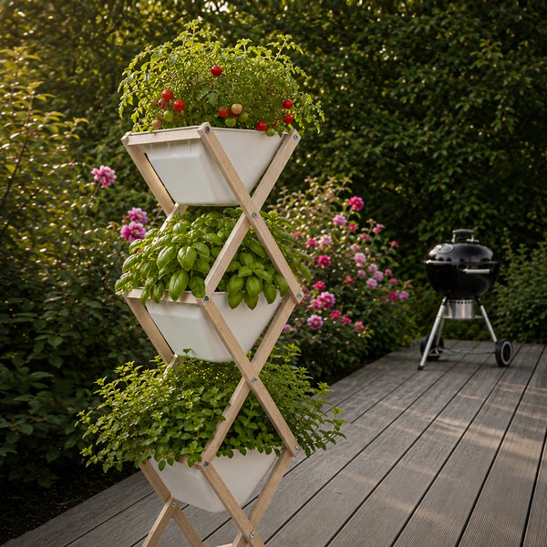 Vertikaler Garten mit Holzrahmen in X-Form und drei weißen Pflanzgefäßen auf einer Terrasse, bepflanzt mit Tomaten und Kräutern neben einem Grill.