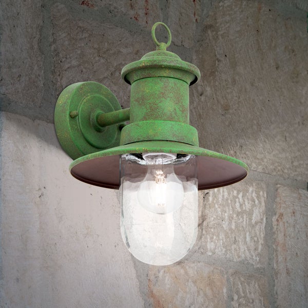 Außenwandleuchte aus Metall mit grüner Patina und klarem Glas an einer Steinwand.