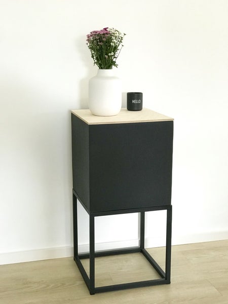 Moderner schwarzer Beistelltisch in Würfelform mit heller Holzplatte und Metallgestell, dekoriert mit einer Blumenvase in hellem Ambiente.