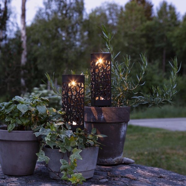 Zwei beleuchtete Gartenlaternen aus Metall neben bepflanzten Blumentöpfen