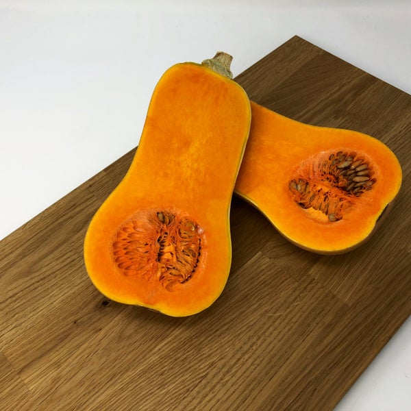 Halbierter Butternut-Kürbis mit Kernen auf einem Holzbrett.