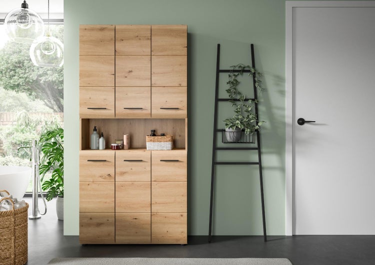 Moderner Badezimmerhochschrank in Eichenoptik mit offenem Fach und schwarzen Griffen in einem hellen Badezimmer.