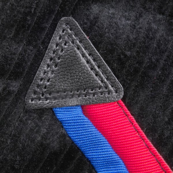 Detailansicht eines dreieckigen Leder-Patches mit Ziernähten auf schwarzem Cordstoff mit blau-rotem Webband.