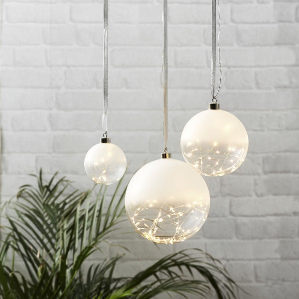 Drei dekorative Kugeln mit Lichtelementen hängen an Bändern vor einer Ziegelwand.