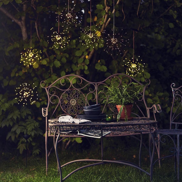 Gartenszene mit Metalltisch, Stuhl, Bank, Geschirr, Topfpflanze und Solarleuchten