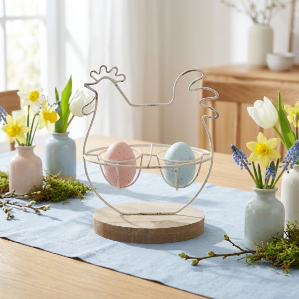 Osterdeko Eierhalter in Huhnform aus Metall mit Holzsockel auf einem Tisch mit Frühlingsblumen