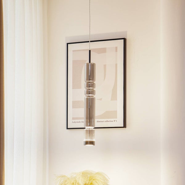 Moderne Pendelleuchte mit einem schlanken, strukturierten Glasschirm vor einem eingerahmten Bild in einem hellen Raum.