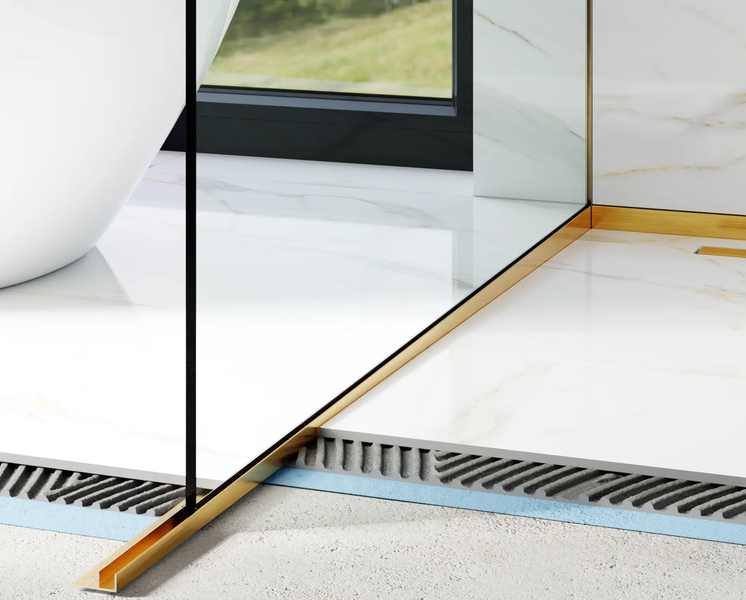 Goldfarbene Fliesenschiene aus Metall als Abschlusskante zwischen Fliesen in Marmoroptik im Badezimmer mit Glasduschtrennwand.