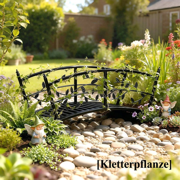 Dekorative Gartenbrücke aus Metall mit Blattornamenten in einer hellen Gartenlandschaft mit Kieselsteinen, Kletterpflanzen und Blumen.