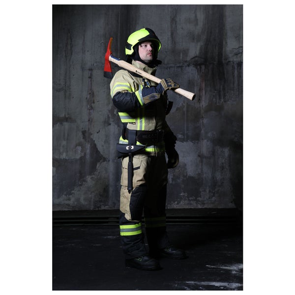 Feuerwehrmann in Schutzkleidung mit Reflexstreifen, Schutzhelm und Feuerwehrbeil vor einer Betonwand.