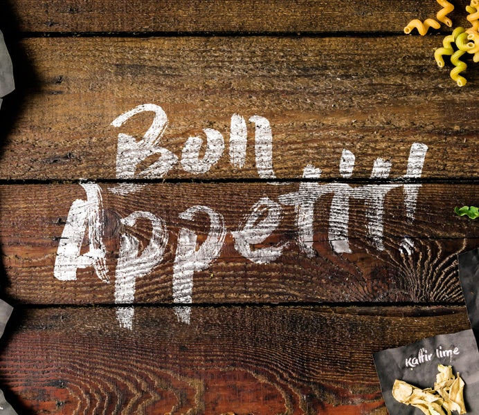 Holztisch mit der Aufschrift Bon Appetit, Pasta und Kräutern