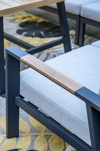 Detailaufnahme eines Garten-Loungesessels mit dunklem Metallgestell, Holz-Inlay an der Armlehne und hellen Polstern.