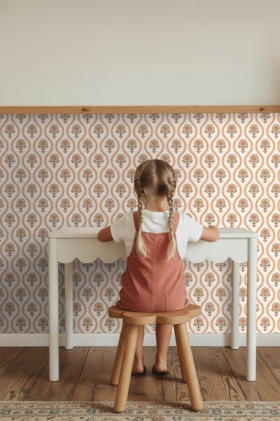 Kind sitzt an einem Schreibtisch vor einer Wand mit gemusterter Tapete