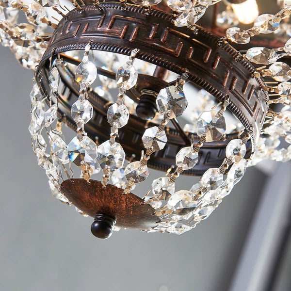Nahaufnahme einer Deckenleuchte mit antik-bronzefarbenem Metallrahmen, Mäander-Muster und Behang aus klaren Kristallglas-Elementen.