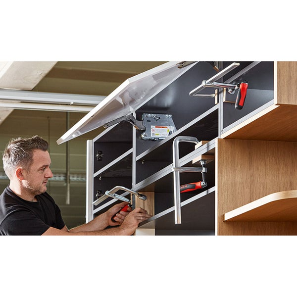 Mann montiert Klappenbeschlag an einem Schrank mit Schraubzwingen.