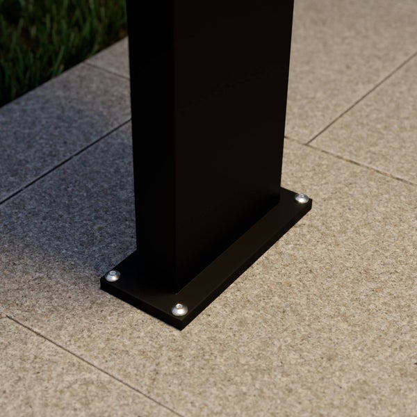 Schwarze Pfostenhalterung mit Grundplatte, verschraubt auf einer Terrasse aus Steinplatten.