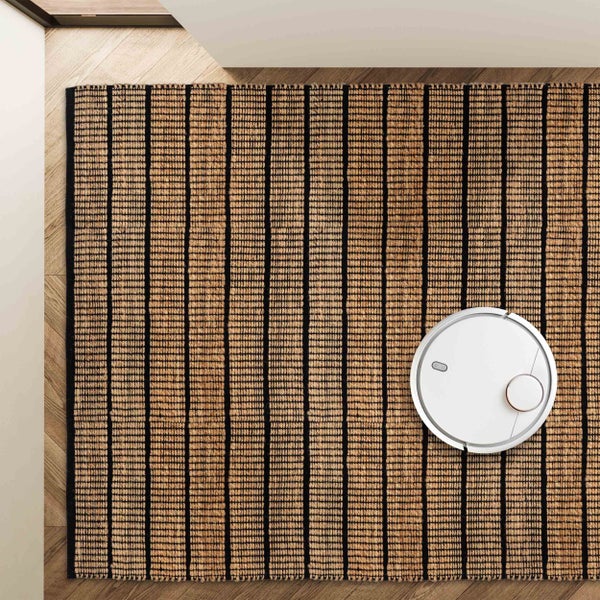 Draufsicht auf einen gewebten Teppich mit schwarzen Streifen auf einem Holzboden mit einem weißen Saugroboter.