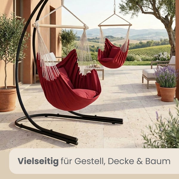Zwei rote Hängesessel aus Stoff auf einer Steinterrasse, einer an einem schwarzen Metallgestell und einer hängend montiert.
